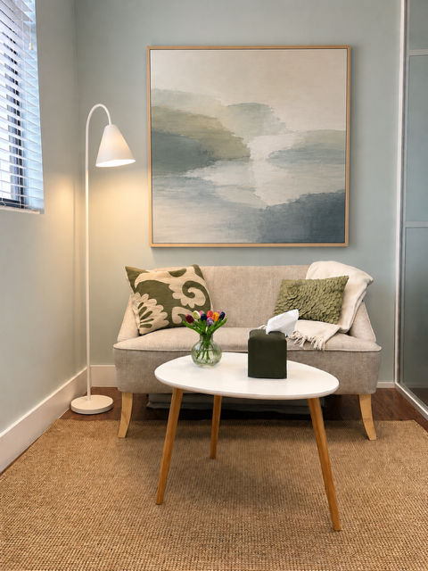 A calm therapy office with a sofa, soft lamp, flowers, and blue-green artwork